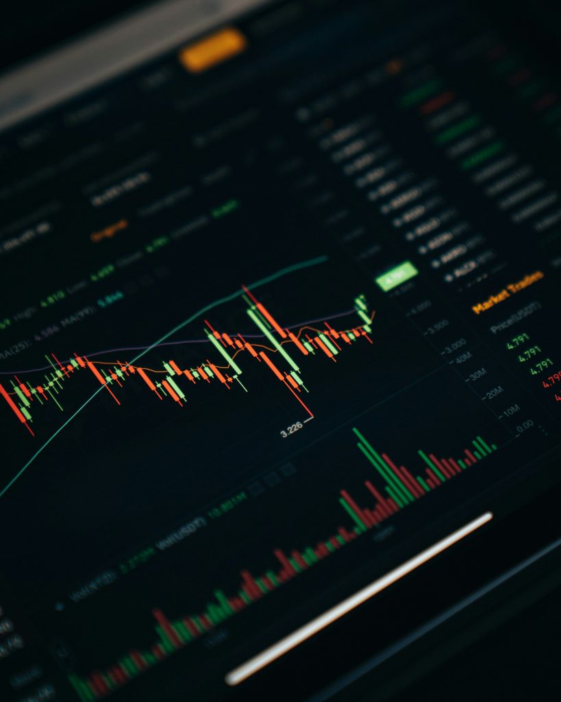 A close-up view of a stock market trading interface with candlestick charts and trading volume bars on a dark background.