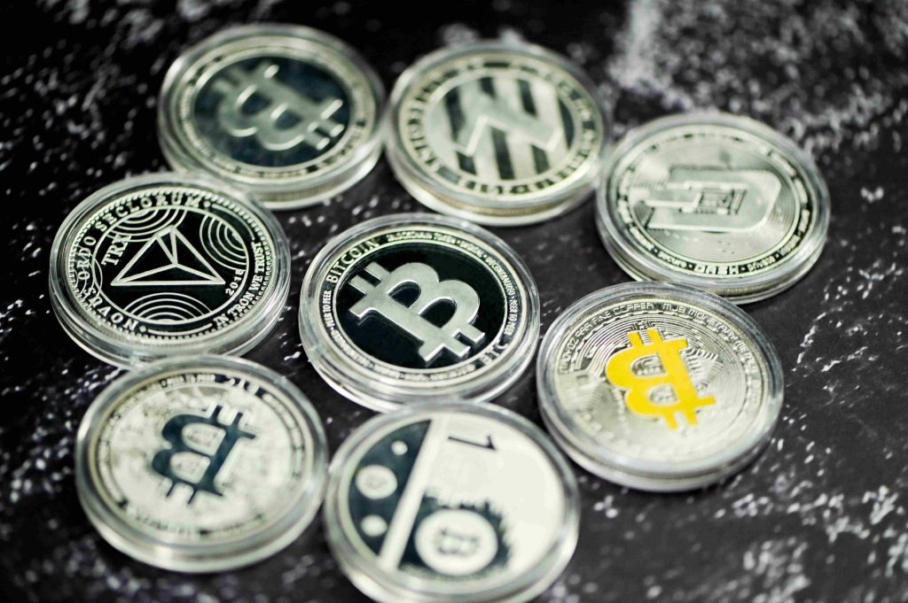 Physical tokens representing various cryptocurrencies, including Bitcoin, Ethereum, and others, arranged on a dark marbled surface.